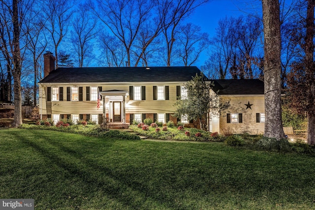 raised ranch featuring brick siding, a chimney, and a front lawn