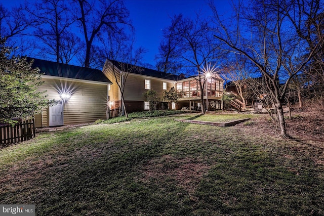 back of house at twilight featuring a yard, stairway, a deck, and fence