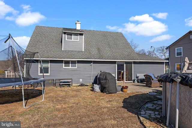 rear view of property featuring a yard, a chimney, a shingled roof, and a trampoline