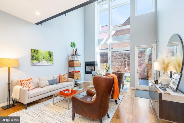 living room featuring recessed lighting, wood finished floors, a multi sided fireplace, a towering ceiling, and baseboards