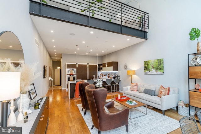 living room with light wood-style flooring, a high ceiling, and recessed lighting