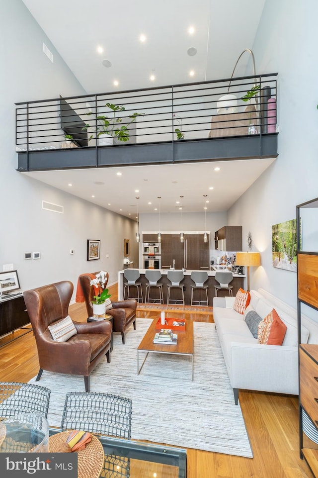 living area with a towering ceiling, visible vents, and wood finished floors