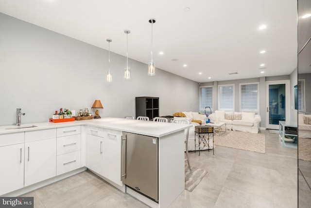 kitchen with refrigerator, a peninsula, light countertops, white cabinetry, and a sink