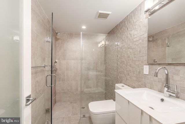 bathroom with a stall shower, visible vents, toilet, vanity, and tile walls