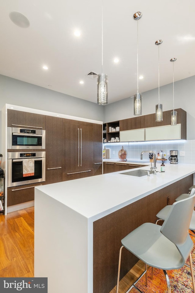 kitchen featuring a breakfast bar, a sink, light wood-style floors, light countertops, and modern cabinets