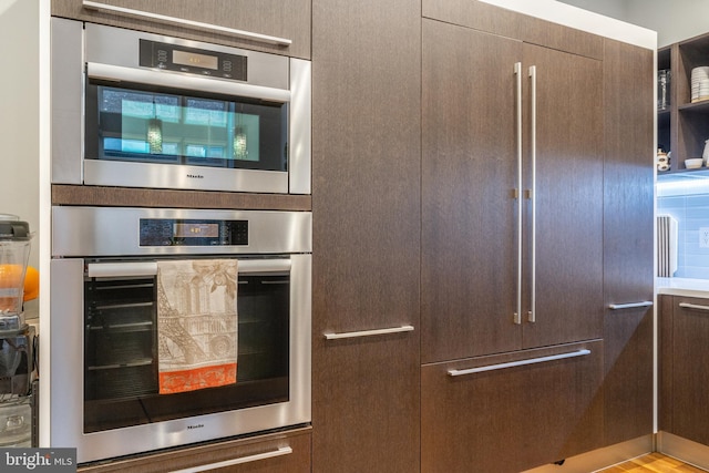 kitchen featuring paneled fridge, stainless steel double oven, and dark brown cabinetry