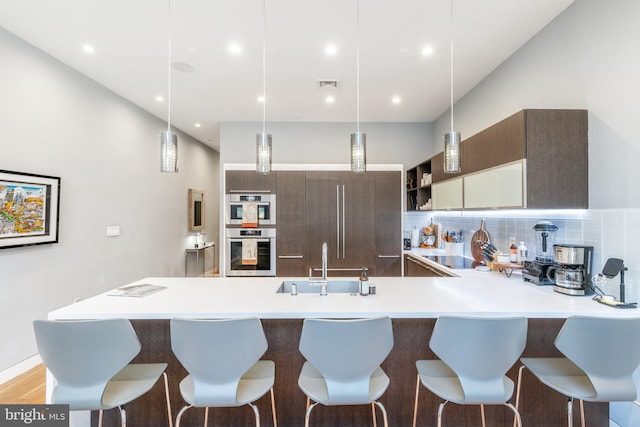 kitchen with visible vents, a peninsula, light countertops, stainless steel double oven, and a sink