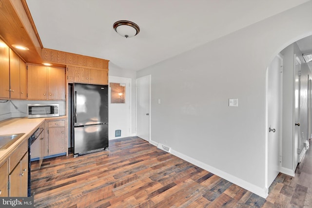 kitchen featuring baseboards, arched walkways, wood finished floors, light countertops, and black appliances