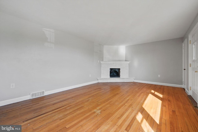 unfurnished living room featuring light wood finished floors, baseboards, visible vents, and a fireplace with raised hearth