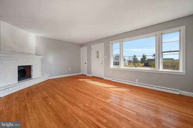 unfurnished living room with a stone fireplace, baseboard heating, light wood-type flooring, and baseboards