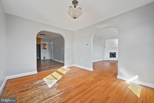 spare room featuring a brick fireplace, baseboards, arched walkways, and hardwood / wood-style floors