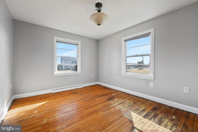 empty room featuring a baseboard heating unit, hardwood / wood-style floors, and baseboards