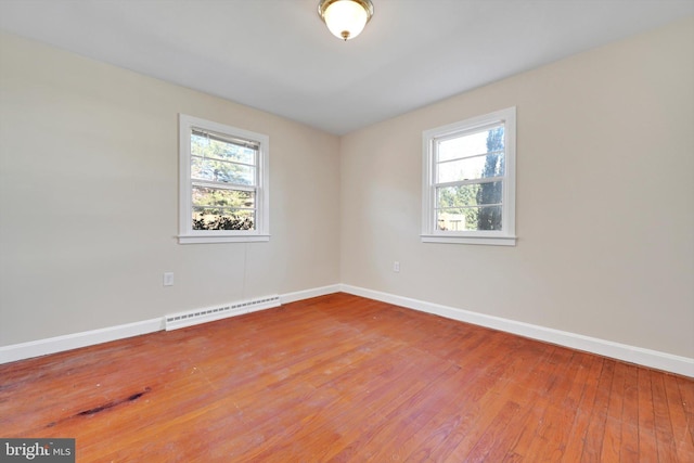 unfurnished room with a baseboard heating unit, a wealth of natural light, wood-type flooring, and baseboards