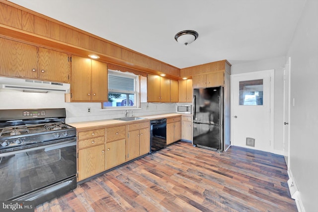 kitchen with light countertops, a sink, wood finished floors, under cabinet range hood, and black appliances