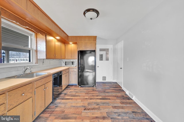 kitchen featuring light countertops, a sink, black appliances, wood finished floors, and baseboards