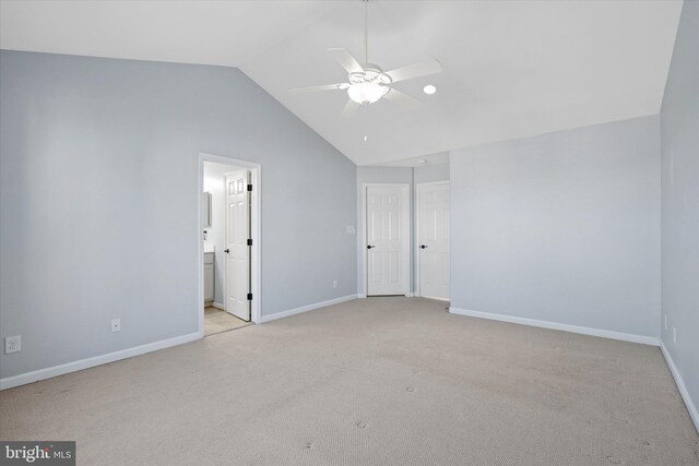 unfurnished bedroom with light colored carpet, a ceiling fan, lofted ceiling, ensuite bath, and baseboards