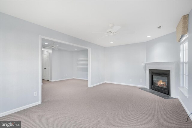 unfurnished living room featuring carpet floors, baseboards, a fireplace with flush hearth, and ceiling fan