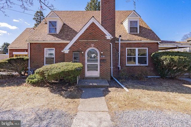 view of front of home with brick siding, a chimney, and a shingled roof