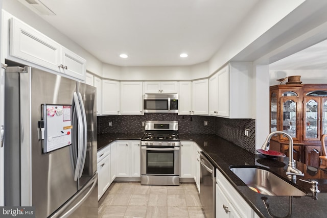 kitchen with stainless steel appliances, dark stone counters, a sink, and backsplash