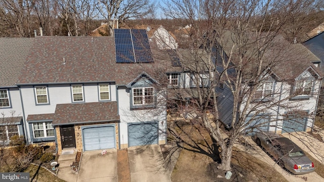 townhome / multi-family property with roof with shingles, driveway, an attached garage, and solar panels