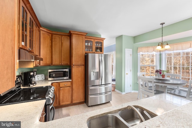 kitchen with a sink, hanging light fixtures, stainless steel appliances, under cabinet range hood, and brown cabinets