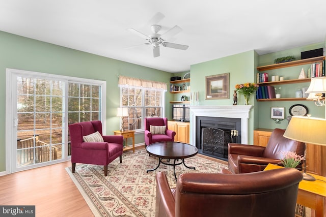 living area with a ceiling fan, light wood-style flooring, a fireplace, and baseboards