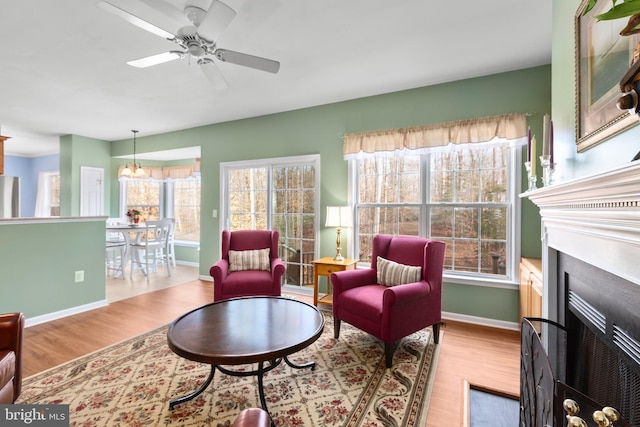 living area featuring a fireplace with flush hearth, wood finished floors, baseboards, and ceiling fan