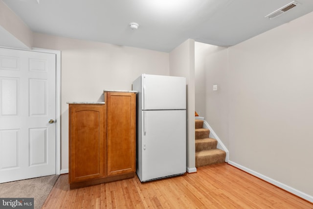 kitchen with brown cabinetry, visible vents, light wood finished floors, baseboards, and freestanding refrigerator