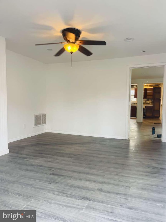 unfurnished room with a ceiling fan, wood finished floors, visible vents, and baseboards