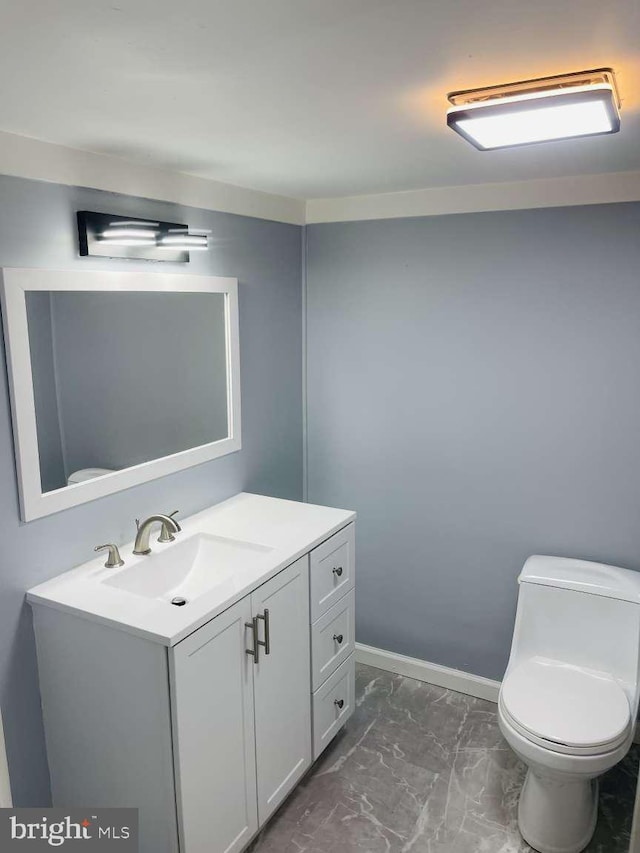 half bathroom featuring toilet, marble finish floor, baseboards, and vanity