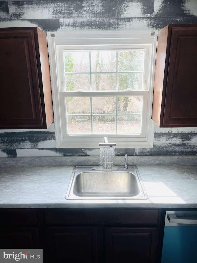 kitchen with dishwashing machine, dark brown cabinets, a sink, and light countertops