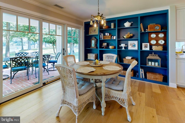 dining space featuring light wood finished floors, an inviting chandelier, visible vents, and crown molding