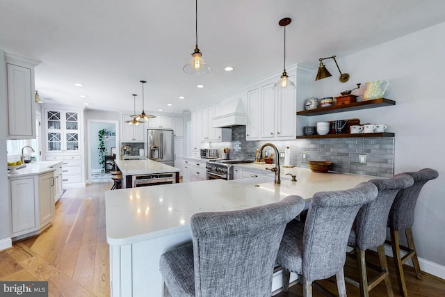 kitchen featuring tasteful backsplash, appliances with stainless steel finishes, light wood-style floors, premium range hood, and a peninsula