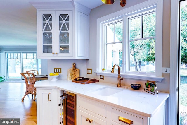 kitchen with light wood-style flooring, glass insert cabinets, white cabinetry, a sink, and beverage cooler