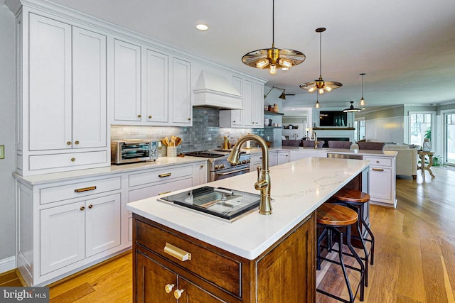 kitchen featuring stainless steel stove, a toaster, premium range hood, open floor plan, and light wood-type flooring