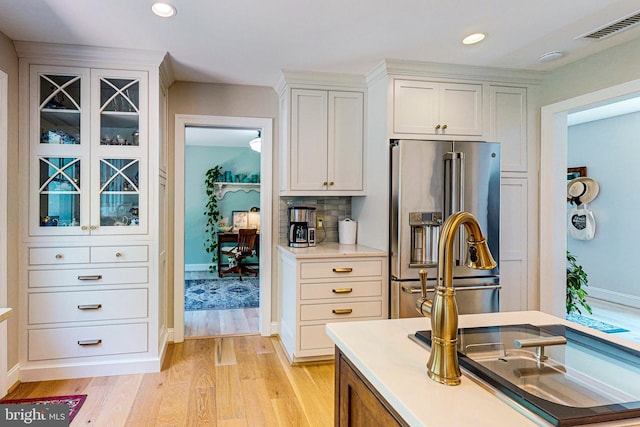 kitchen featuring stainless steel refrigerator with ice dispenser, light wood finished floors, tasteful backsplash, visible vents, and white cabinets