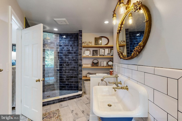 bathroom with recessed lighting, a tile shower, tile walls, and a sink