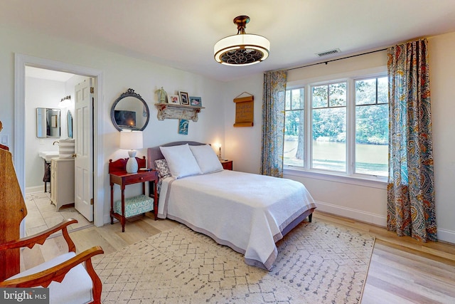 bedroom featuring light wood-type flooring, baseboards, visible vents, and ensuite bathroom