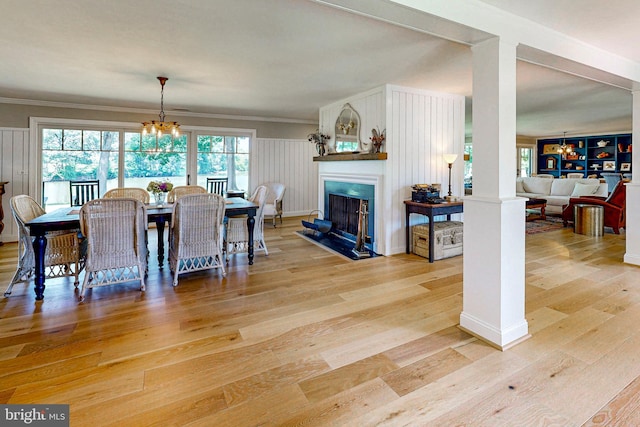 dining room with light wood-style floors, a fireplace with flush hearth, crown molding, ornate columns, and a chandelier