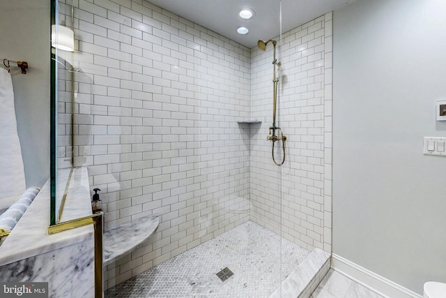 full bath with marble finish floor, a tile shower, and baseboards