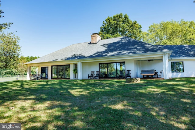 back of property with roof with shingles, a chimney, a ceiling fan, and a yard