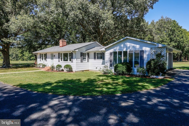 single story home featuring aphalt driveway, fence, roof with shingles, a front lawn, and a chimney