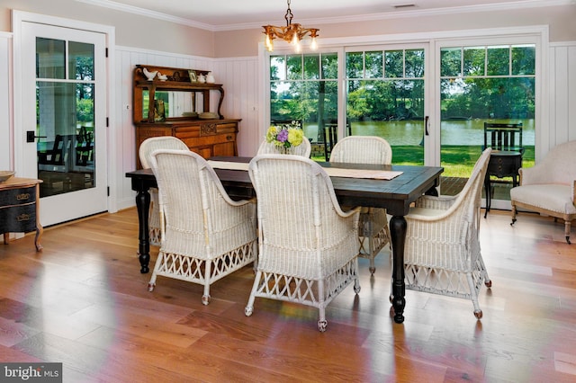 dining area with a water view, visible vents, light wood-style floors, ornamental molding, and an inviting chandelier