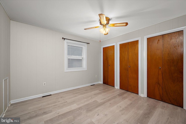 unfurnished bedroom with visible vents, light wood-style floors, multiple closets, and ornamental molding