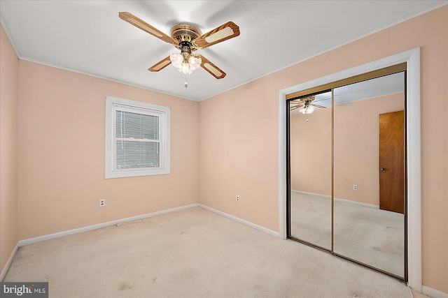 unfurnished bedroom with ornamental molding, a closet, carpet, baseboards, and ceiling fan