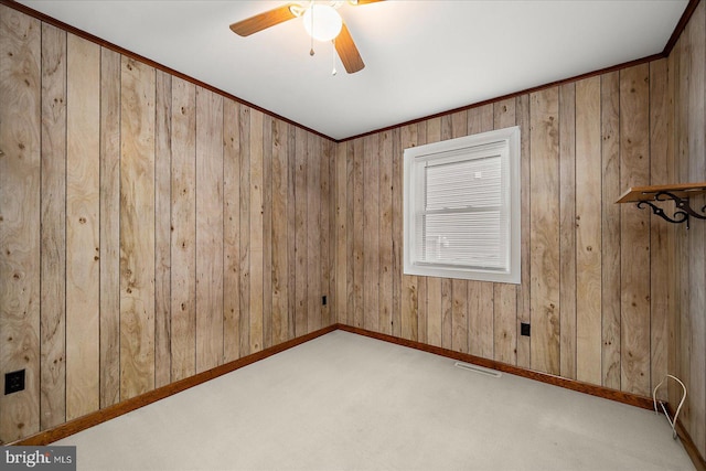 carpeted spare room with wooden walls, visible vents, baseboards, and a ceiling fan