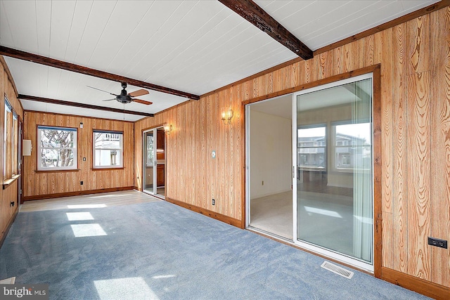 spare room with beamed ceiling, carpet flooring, visible vents, and wood walls