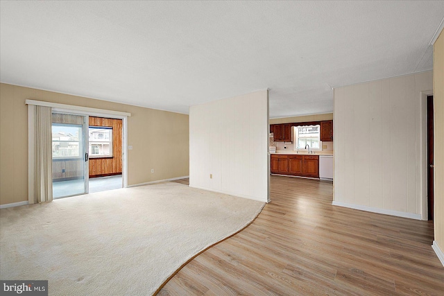 unfurnished living room with a sink, baseboards, light colored carpet, and light wood-style flooring