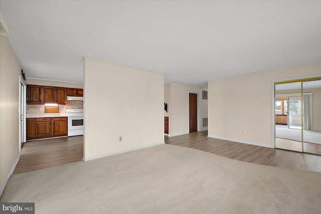 unfurnished living room featuring carpet flooring, wood finished floors, and visible vents