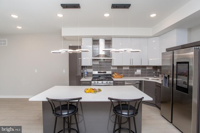 kitchen featuring a breakfast bar area, stainless steel appliances, a sink, modern cabinets, and wall chimney exhaust hood